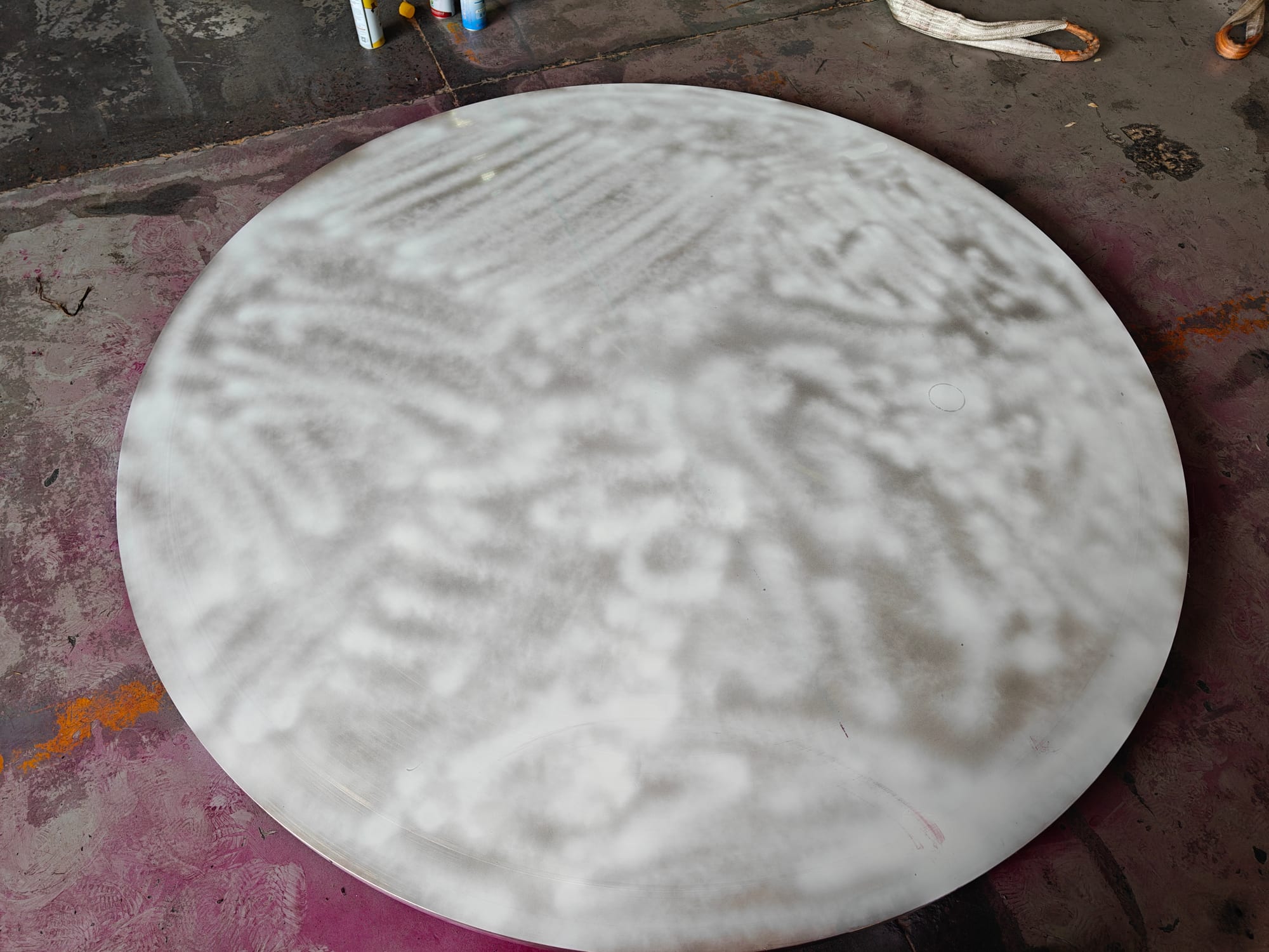 Forged disc coated with white developer during a penetrant examination, penetrant cans alongside