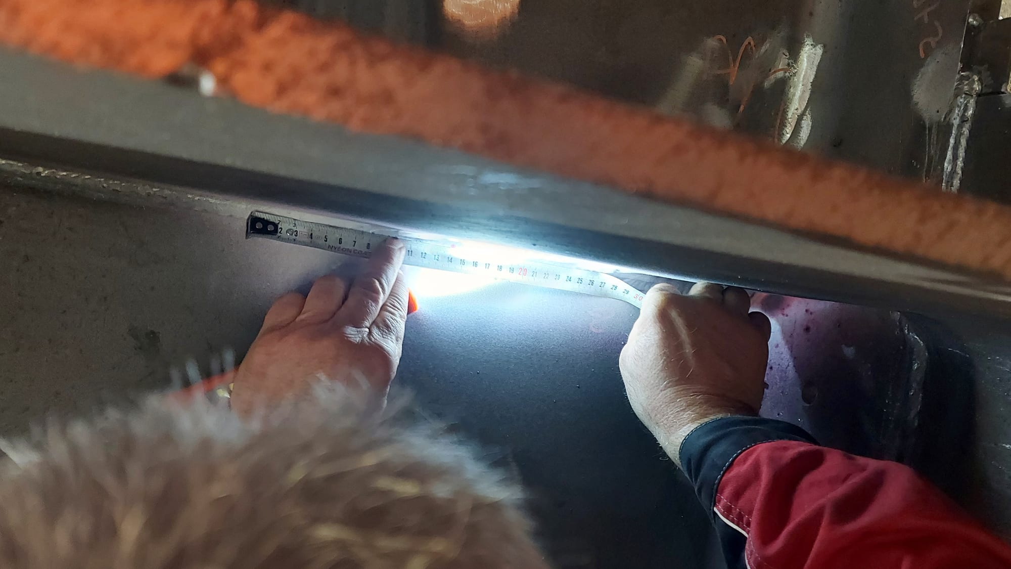 Inspectors measuring a penetrant indication on a welded steel member under a torch